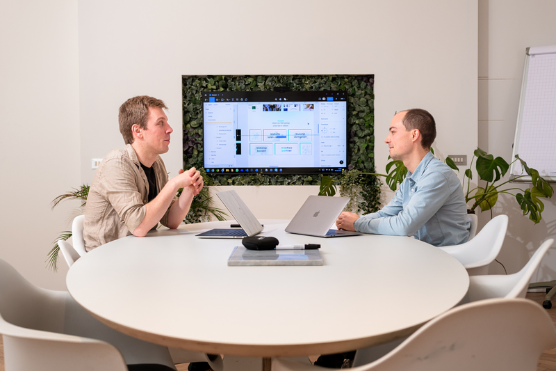 Twee teamleden van upshift bespreken samen een digitaal project aan tafel.